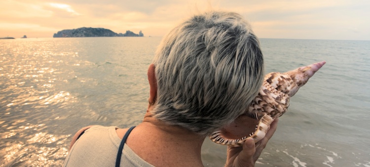 Senior listening to a seashell on the beach